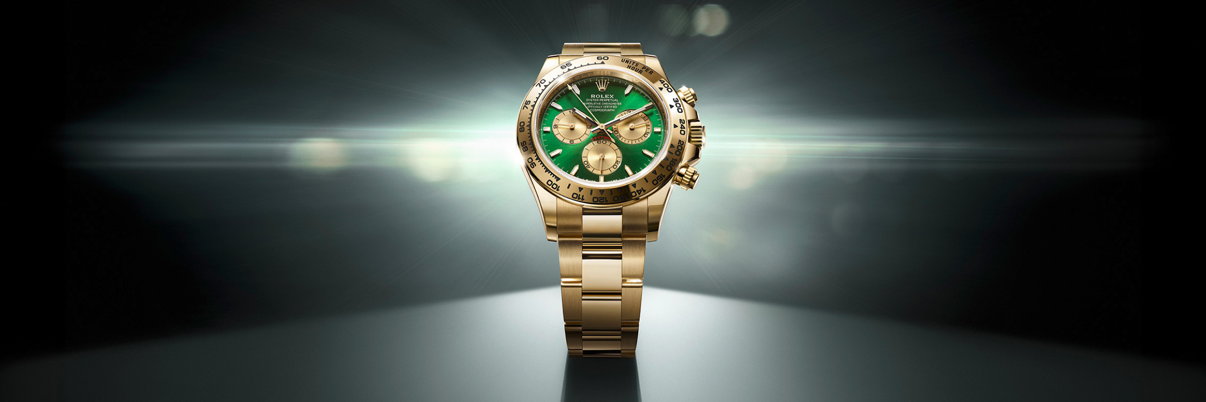 Rolex Cosmograph Daytona in yellow gold with green dial spotlighted against a dark gradient background