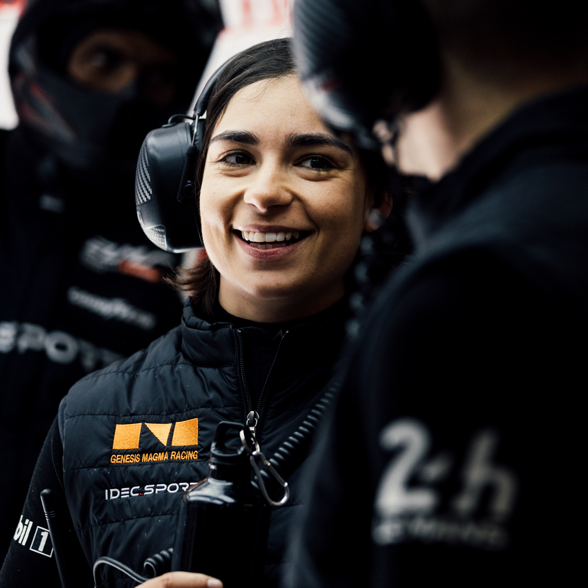  Jamie Chadwick smiling in racing gear, wearing a headset in the team garage during an endurance event.